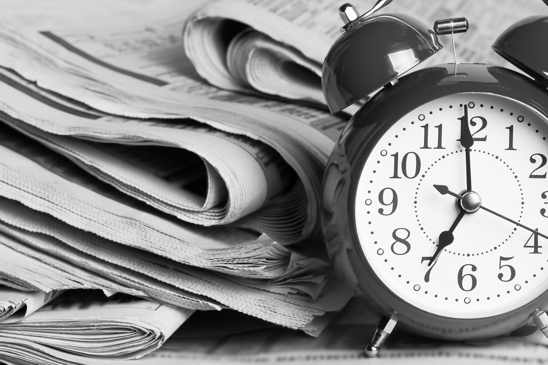 Alarm clock sitting next to a stack of news papers