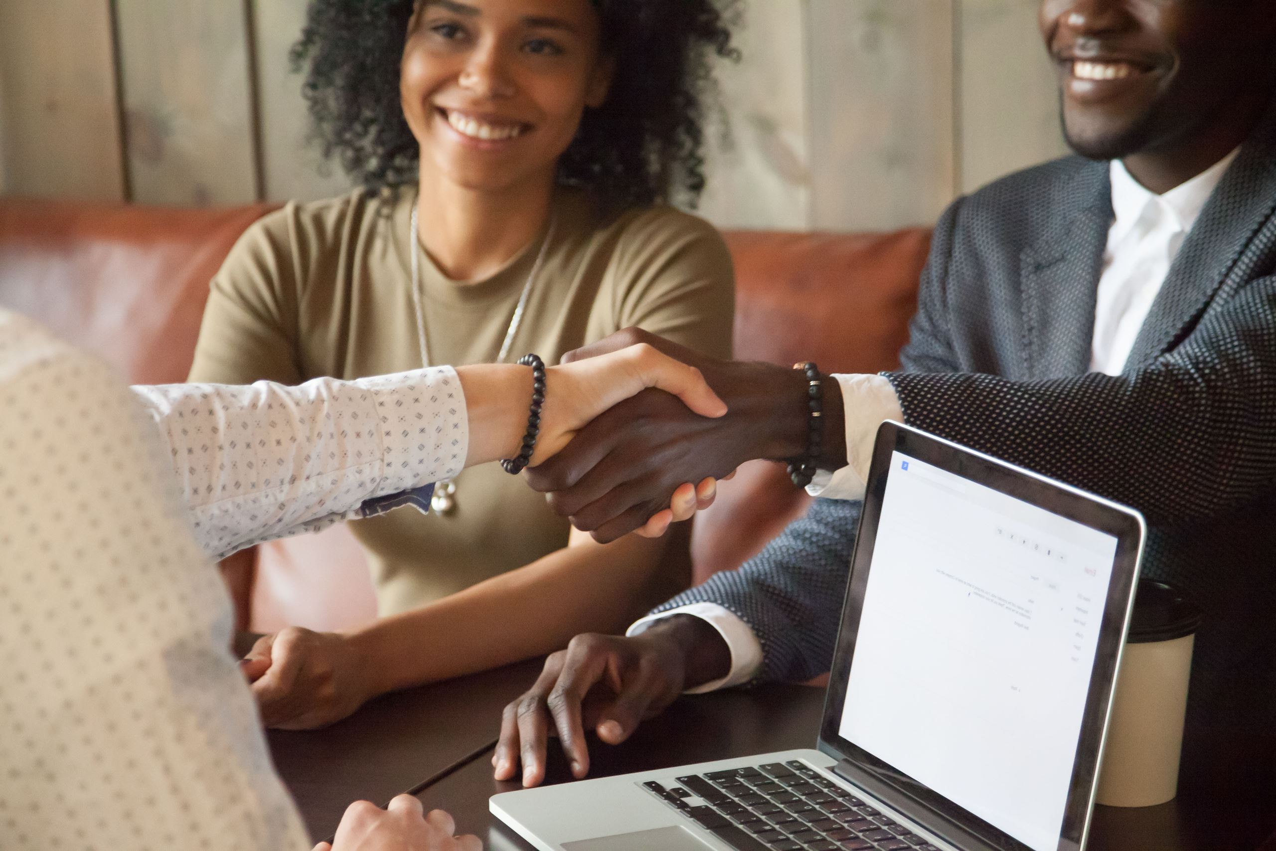 Man and woman, man is shaking hands with another man who is viewing a computer.