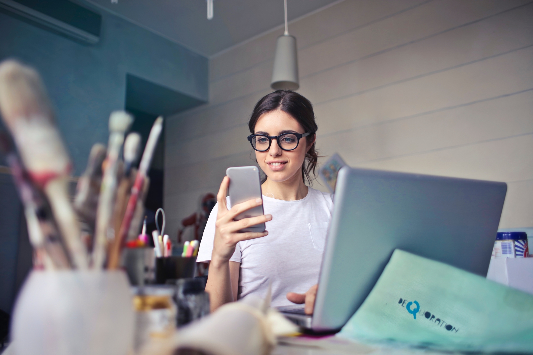 woman holding cell phone working on laptop